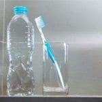 Bottled water with fluoride on counter next to glass with a toothbrush in it