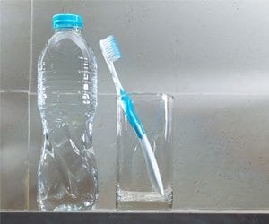 Bottled water with fluoride on counter next to glass with a toothbrush in it