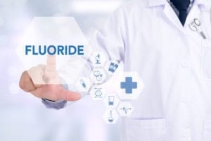 close-up van de romp van een arts die een witte jas draagt ​​en naar de afbeelding van fluoride wijst met medische symbolen zoals een kruis, microscoop en verband • Foto in sectie 5.2 over flessenwater